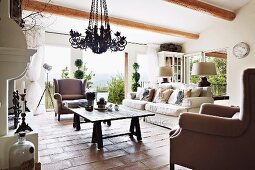 Polstersessel und Sofa um rustikalen Holztisch auf Terrakottaboden in ländlichem Wohnzimmer
