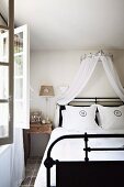 Doppelbett mit schwarzem Metallgestell und Baldachin aus weißem, luftigem Stoff in ländlichem Ambiente