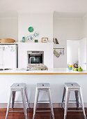 Vintage, industrial-style stools at island counter and oven integrated into half-height wall panelling