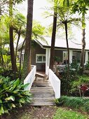 Steg über Bach mit weisssem Holzgeländer vor Wochenendhaus in tropischer Umgebung