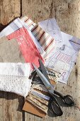 Stoffreste, Borten und Schneiderschere mit Skizzen für selbstgenähten Beutel auf sonniger Holzbank