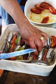 Bread-stuffed anchovies and tomatoes being placed in a dish