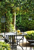 Erfrischungsgetränk auf Gartentisch mit passenden Stühlen aus Metall und am Baum aufgehängte Laternen in sonnigem Garten