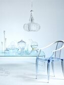 Nicht wirklich - Glasbehälter auf transparentem Tisch und Stuhl aus Acrylglas unter Hängeleuchte aus lamellenförmigem Schirm