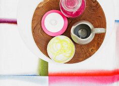 Kitchenware on olive wood platter on table cloth with diffuse stripes of colour