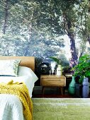 Photo wallpaper with forest motif in bedroom; matching accessories such as plant arrangements and floral print pillows