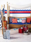 Beach atmosphere - pouffes and anchor ornament in front of wicker bench with various cushions below canopy and in front of wave motif painted on wall