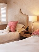 Twin beds with Oriental-style, upholstered headboards next to window with closed, interior shutters