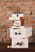 Stacked, white boxes with attached gaming pieces and dice against rustic brick wall