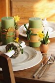 Green candles wrapped in decorative ribbons and place settings with Easter decorations on wooden table