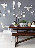 Candles, pots of herbs, crockery and salad on table in front of grey wall with white, decorative brackets