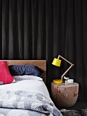 Geschliffener Baumstamm als Nachttisch mit gelber Designer Schreibtischlampe neben Bett