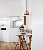 Modern, converted split-level area with solid balustrade; breakfast bar, wooden bar stools and copper pendant lamp in foreground