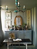 Chandelier above table in front of collection of goblets on farmhouse sideboard; framed floral pictures on wall