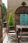 French wire chairs, monastery table and artistic, delicate, Indian iron window in courtyard with floor made from large concrete slabs and gravel strips