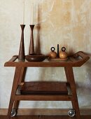 Artistic wooden vessels and candlesticks and stack of leather, patchwork table mats on serving trolley against antique, marbled wall
