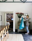 Woman in front of chest of drawers in dining area next to open double doors with view into living room