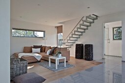 Chaise sofa against wall with ribbon of transom windows in open-plan interior with staircase; platform with glossy tiles in foreground