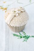 A celebratory cupcake decorated with sugar pearls and sugar flowers