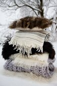 Gestapelte Wolldecken, Felle und ein Kissen mit Pelzbezug im Schnee