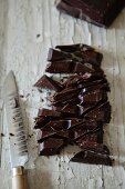 Zerkleinerte dunkle Schokolade auf Holztisch, daneben Messer
