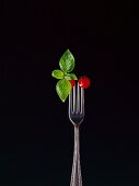 Basil and two cocktail tomatoes skewered on a fork