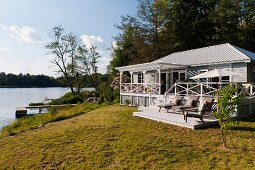 Zu Wochenendhaus ausgebaute Fischerhütte im weissen Long- Island-Stil am See; Plattform mit Liegestühlen und überdachte Eingangsveranda