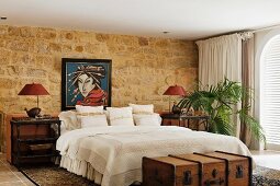 Pleasant bedroom with exotic mood provided by steamer trunk, colonial-style tables and Japanese portrait over comfortable double bed