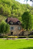 Idyllisch gelegenes Mühlengebäude mit Teich vor bewaldetem Hügel in der Dordogne