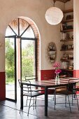 Delicate metal chairs around table in corner of room with open, arched, glass double doors and view into garden