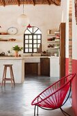 Sessel mit roter Seilbespannung und Metallgestell auf Estrichboden vor minimalistischem Kochbereich