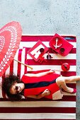 Red girls' accessories and toys on red and white striped rug; smiling girl in red dress lying on rug