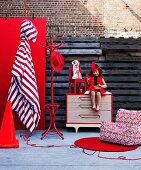 Bright red home accessories and furniture with little girl in red dress sitting on chest of drawers