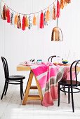 Cheerful tablecloth on dining table below copper pendant lamp and garland of shiny paper tassels