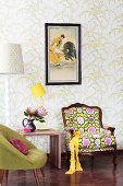 Fifties chair, bright postmodern armchair and yellow table lamp on stool against wall with floral wallpaper
