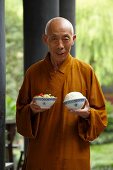 A monk with a bowl of rice and a bowl of vegetables