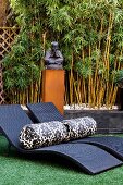Bolsters on dark wicker sun loungers in front of statue of Buddha and stand of bamboo against wall