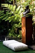 Floor cushions on artificial grass in front of statue of Buddha and tall ferns