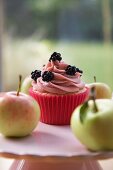 Cupcake mit Brombeeren, umgeben von frischen Äpfeln