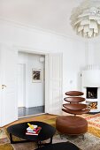 Black metal coffee table in front of classic office chair with brown leather cover and matching footstool; open double doors in background next to white corner fireplace