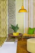 House plant on wooden table, yellow chair and pouffe in front of lengths of wallpaper