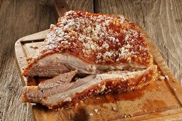 Roast pork belly on a chopping board (partly sliced)