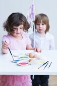 Little girl painting Easter eggs with second child watching