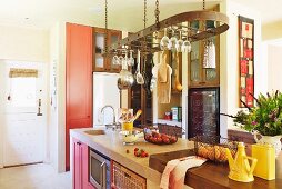 Modern, country-house kitchen with kitchen utensils hanging from rack above island block