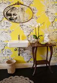 Modern sink and wooden console table with curved legs against yellow wallpaper with large urn motif