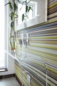 Candle lanterns on transparent, plexiglass console table against wall decorated with horizontal, coloured stripes