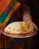 A woman holding a plate with a cheese naan (India)