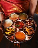 A woman holding a tray of assorted sauces from India