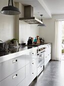 Long kitchen counter with stainless steel worksurface and pendant lamps with metal lampshades