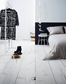 Einfaches, minimalistisches Schlafzimmer mit weißem Holzdielenboden und Kleiderstange mit schwarz-weißem Kleid